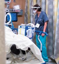 Healthcare worker in protective gear checking on a patient in a hospital room.